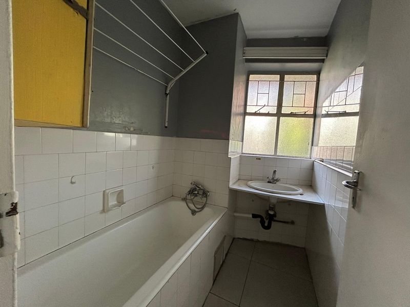 A compact bathroom featuring a bathtub, wall-mounted basin, and tiled finishes. The space is in need of cosmetic updates and modernization.
