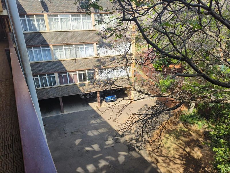 View of the apartment building rear facade featuring brick exterior, covered parking bays, and paved driveway area.