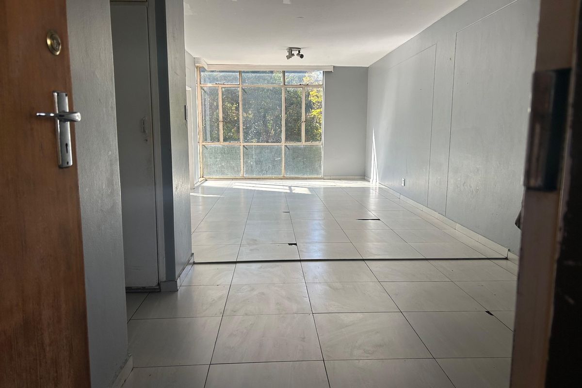 An empty, open-plan living area featuring large windows and tiled flooring, requiring minor repairs to the floor surface.