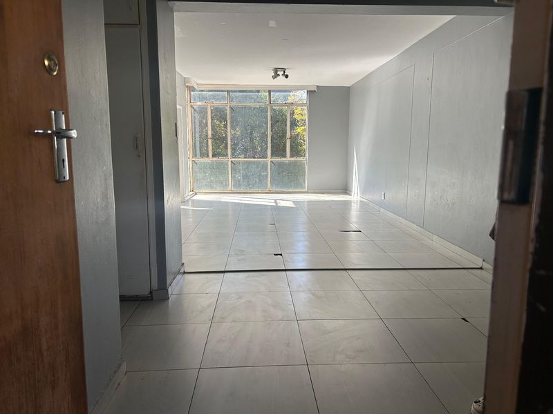 An empty, open-plan living area featuring large windows and tiled flooring, requiring minor repairs to the floor surface.