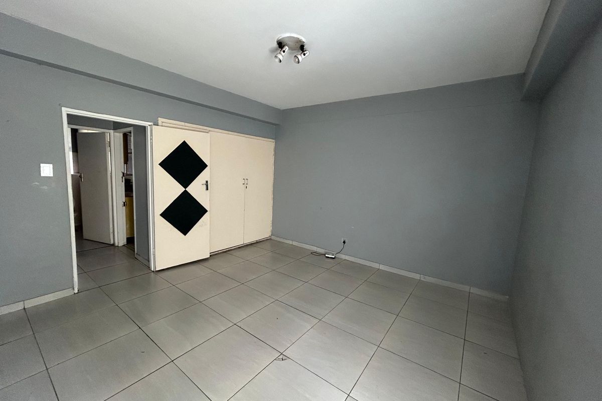 An empty bedroom featuring neutral grey walls, tiled flooring, and built-in storage cupboards with a unique decorative design.