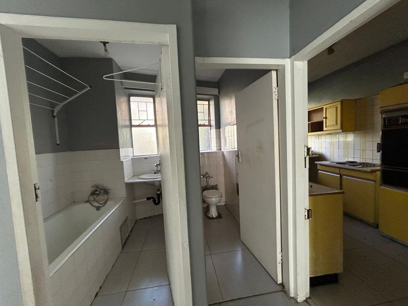 A view from the hallway looking into a bathroom, separate toilet, and kitchen area featuring dated cabinetry and original fixtures.