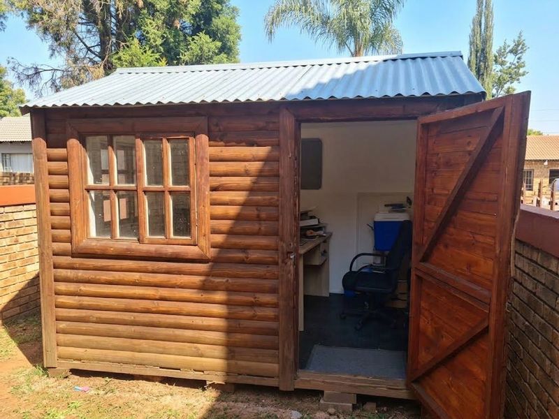 A detached timber log cabin utility space featuring a corrugated metal roof and a timber-framed window, suitable for storage or a home office.