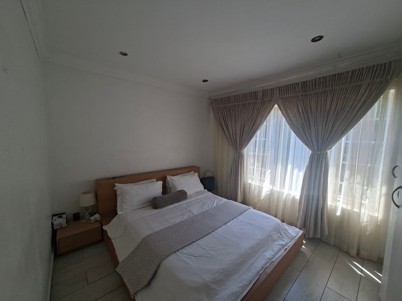 A bedroom featuring tiled flooring, recessed downlighting, and large windows with fitted curtain tracks.