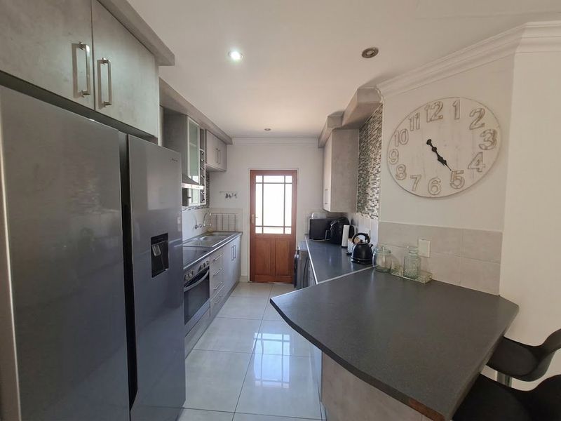 A functional kitchen featuring modern grey cabinetry, dark laminate countertops, tiled flooring, and a convenient breakfast bar area with direct exterior access.