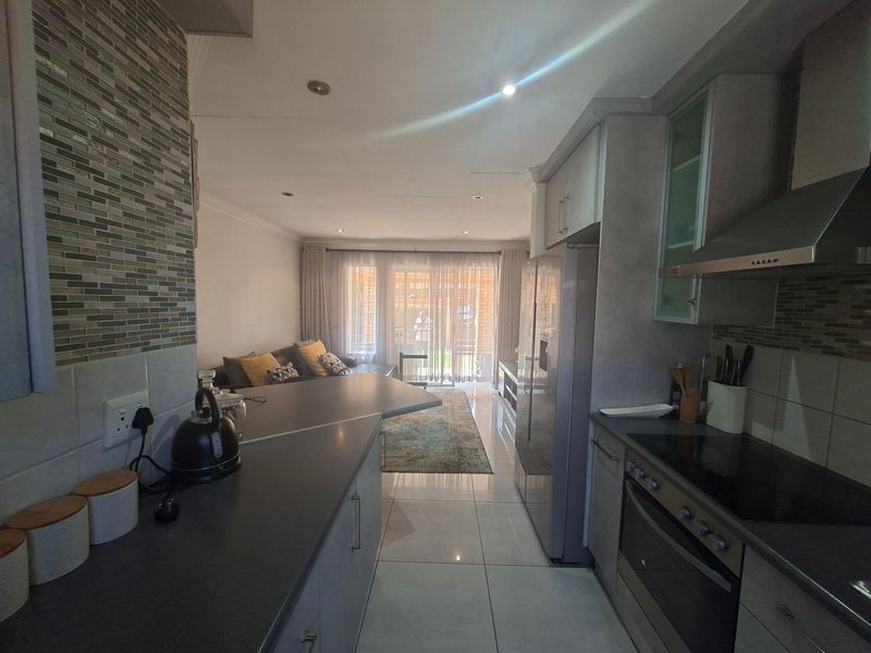 Open-plan kitchen and living area featuring modern cabinetry, integrated appliances, tiled flooring, and direct access to an outdoor patio space.