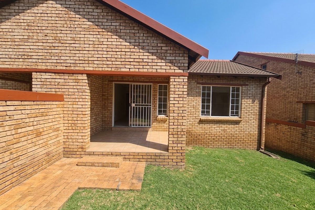 Rear view of the townhouse featuring a face brick facade, a covered patio area, and a private garden with a paved walkway.
