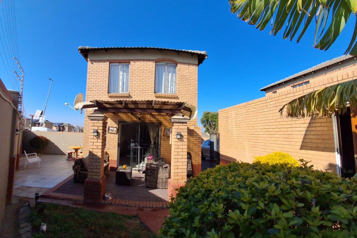 Rear view of a two-story brick townhouse featuring a covered patio area, paved courtyard, and secure perimeter walling.