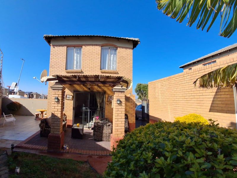 Rear view of a two-story brick townhouse featuring a covered patio area, paved courtyard, and secure perimeter walling.