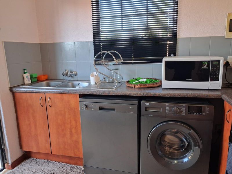 A functional kitchen area featuring built-in cabinetry, a double sink, tiled backsplash, and space for under-counter appliances.