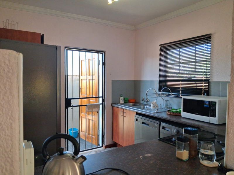 Functional kitchen featuring laminate countertops, built-in cabinetry, a stainless steel sink, and direct access to an exterior area via a security gate.
