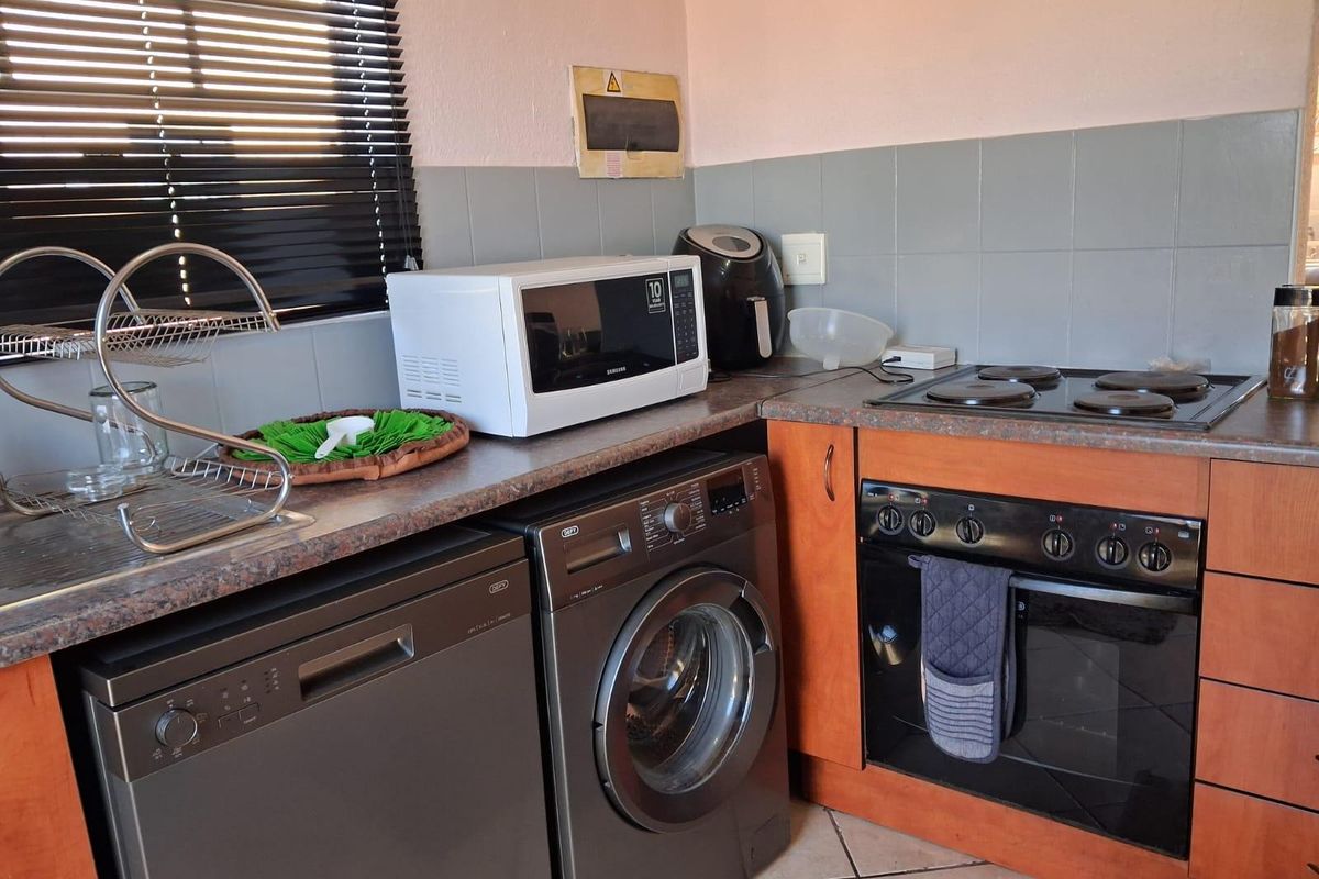 Compact kitchen featuring wood-look cabinetry, tiled backsplash, built-in oven, and electric hob, providing a functional workspace with integrated appliance connections.