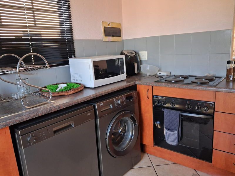 Compact kitchen featuring wood-look cabinetry, tiled backsplash, built-in oven, and electric hob, providing a functional workspace with integrated appliance connections.