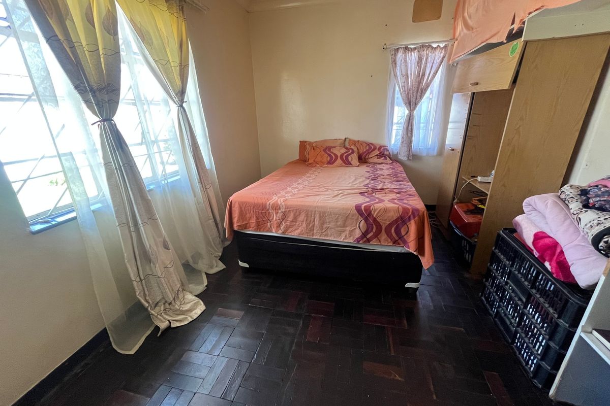 A bedroom featuring dark parquet flooring and security bars on the windows, requiring cosmetic updates to improve the overall finish.