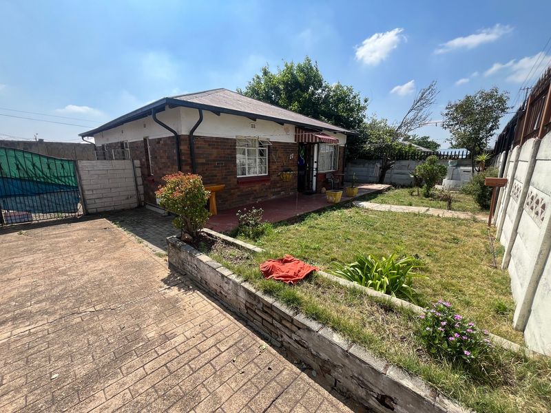 Front view of a single-story brick house featuring a paved driveway, small garden area, and concrete boundary walling.