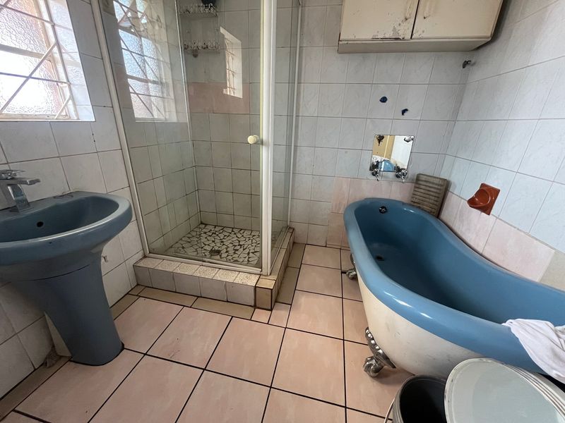 A dated bathroom featuring a blue pedestal basin, a clawfoot bathtub, and a separate shower enclosure with tiled finishes throughout.