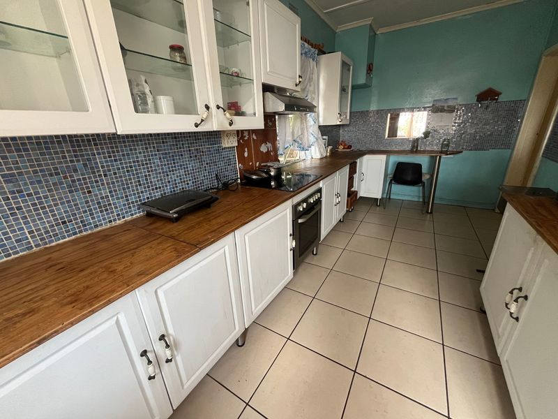 A functional kitchen featuring white cabinetry, wooden countertops, mosaic tile backsplash, and ceramic floor tiles, offering a dated aesthetic ready for modernization.