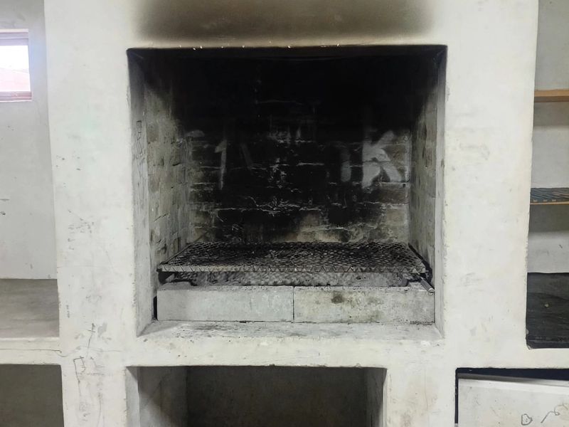 A rustic built-in outdoor braai area featuring a masonry firebox and integrated concrete preparation counters, requiring cosmetic refurbishment.