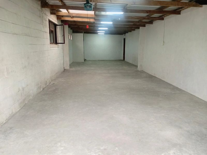A spacious, empty garage featuring exposed timber rafters, concrete flooring, and blockwork walls, offering versatile storage or workshop potential.