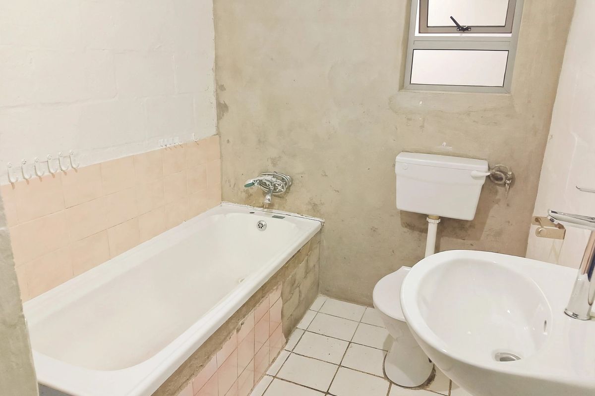 A bathroom featuring a bathtub, toilet, and washbasin, currently requiring finishing work on the walls and tiling to complete the space.