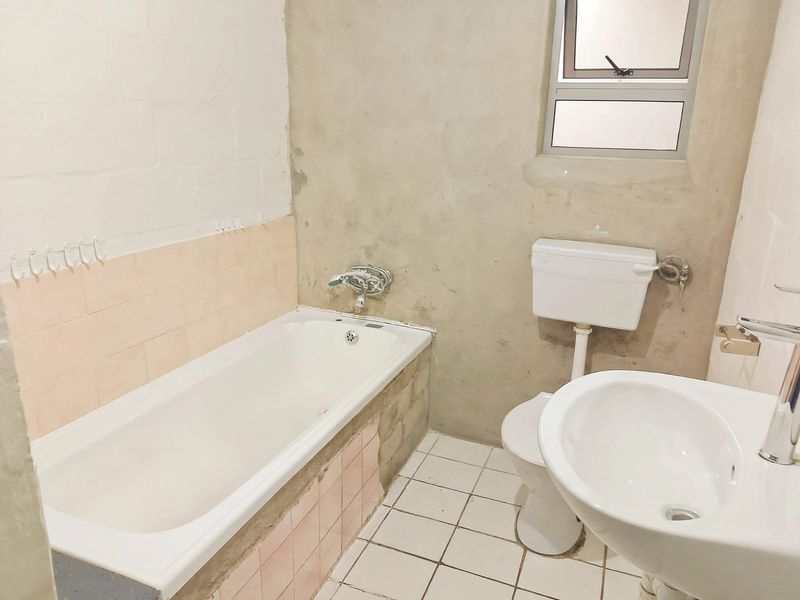 A bathroom featuring a bathtub, toilet, and washbasin, currently requiring finishing work on the walls and tiling to complete the space.