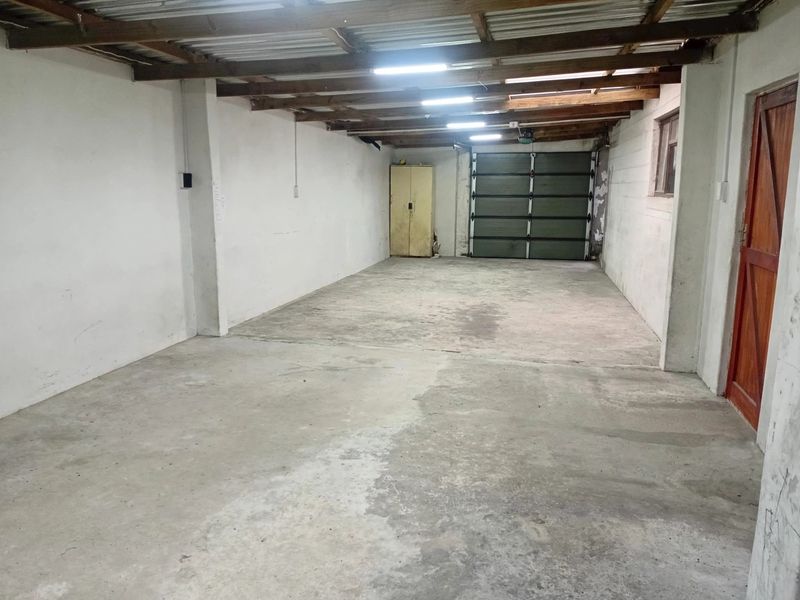 A spacious, empty garage featuring exposed timber rafters, concrete flooring, and a sectional garage door, offering ample storage or parking space.