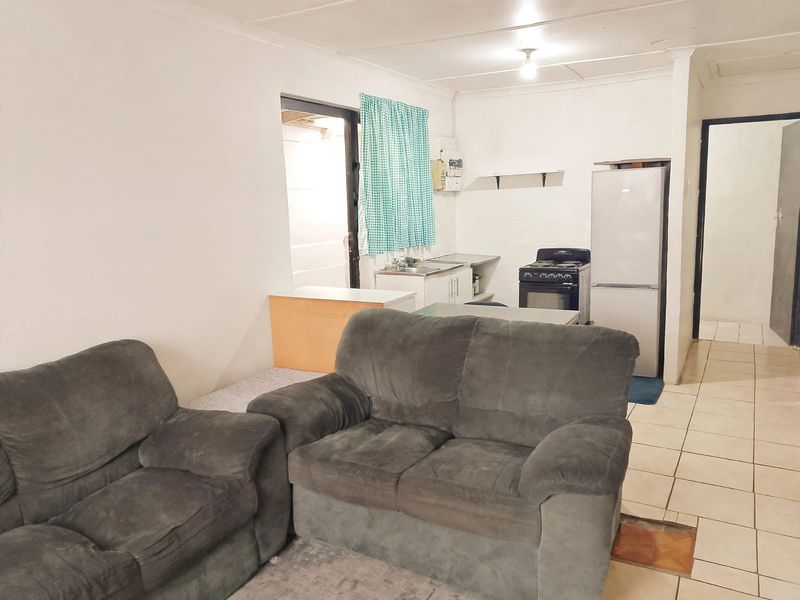 Open-plan living and kitchen area featuring tiled flooring, a basic kitchenette with a sink, and a freestanding stove.
