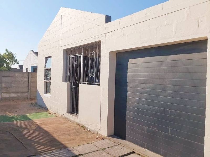 Front exterior view of a single-story house featuring a garage, security gates, and a concrete block boundary wall.