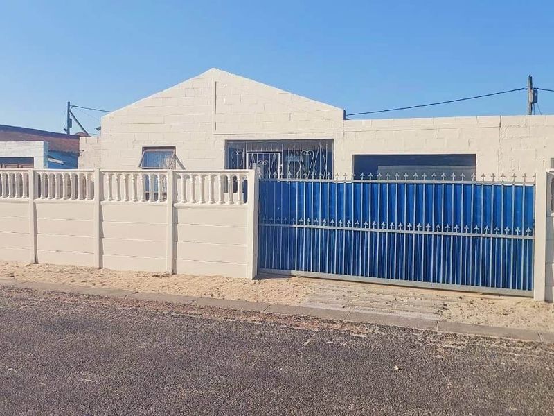 Front exterior view of a single-story house featuring a secure metal gate, precast concrete boundary wall, and security bars on windows.