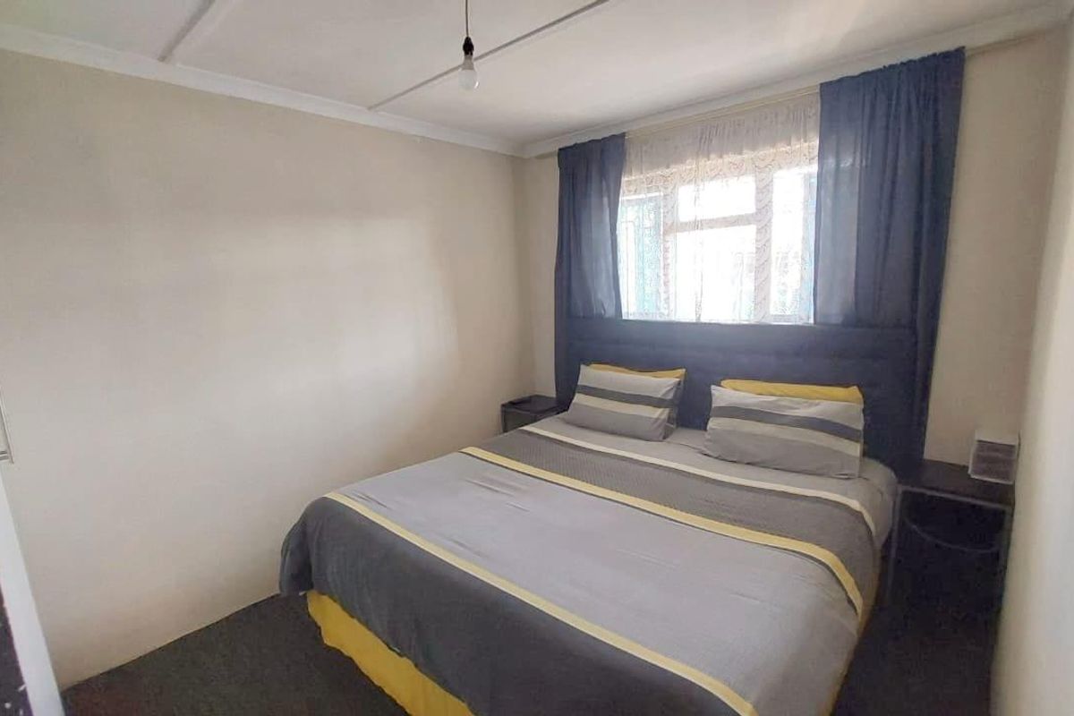 A functional bedroom featuring neutral walls, a built-in cupboard, and a window with curtains, providing a comfortable and practical sleeping space.