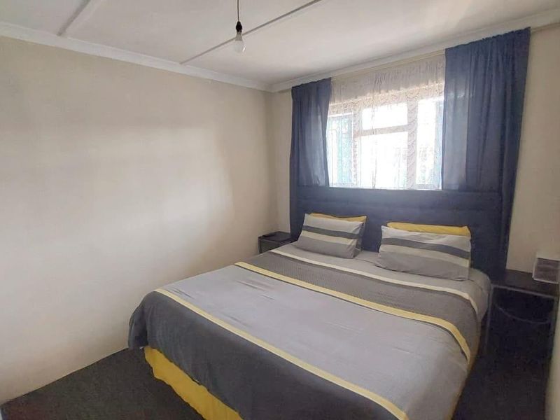 A functional bedroom featuring neutral walls, a built-in cupboard, and a window with curtains, providing a comfortable and practical sleeping space.