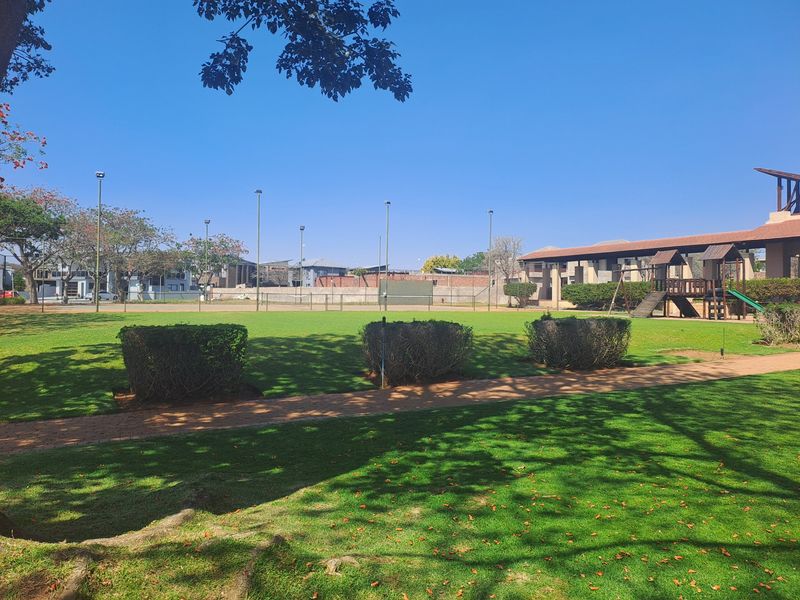 A well-maintained communal garden area featuring manicured lawns, paved pathways, trimmed hedges, and integrated playground equipment for residents.