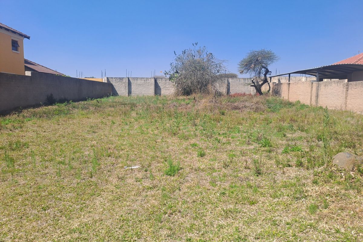 A vacant residential plot featuring perimeter brick boundary walls and natural grass coverage, suitable for future development.