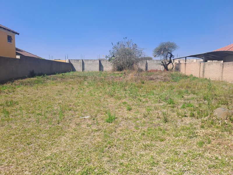 A vacant residential plot featuring perimeter brick boundary walls and natural grass coverage, suitable for future development.