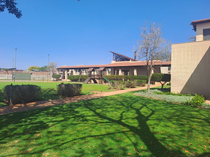 A well-maintained residential garden featuring a manicured lawn, paved pathways, and established perimeter fencing within a secure estate setting.