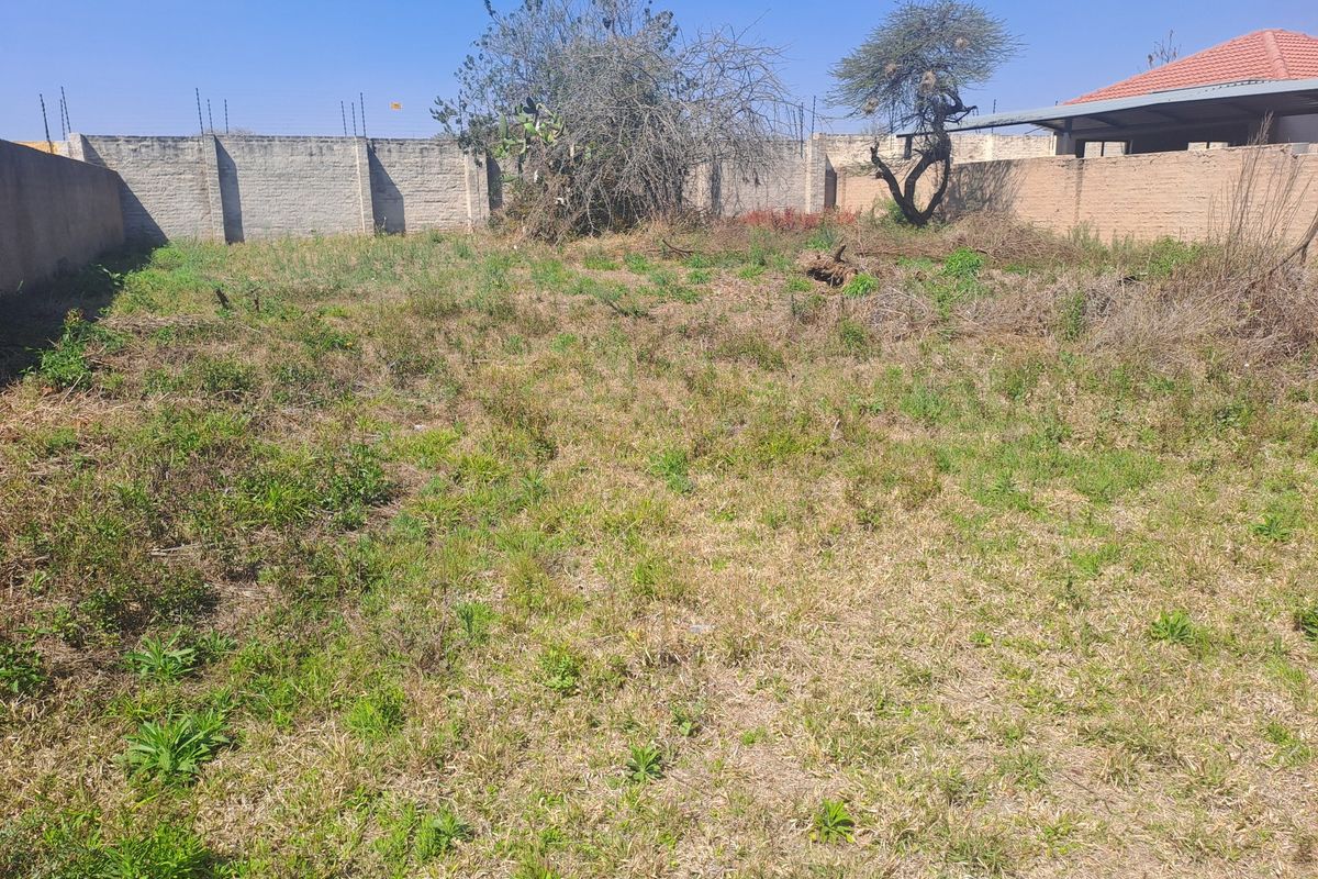 A vacant residential plot featuring perimeter walling with electric fencing and established trees, offering a blank canvas for development.