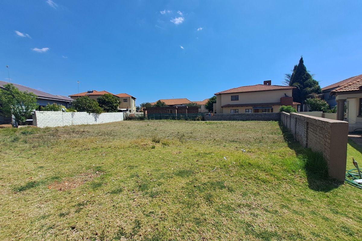 A vacant residential plot featuring a grass lawn and perimeter brick boundary walls, situated within an established residential neighborhood.