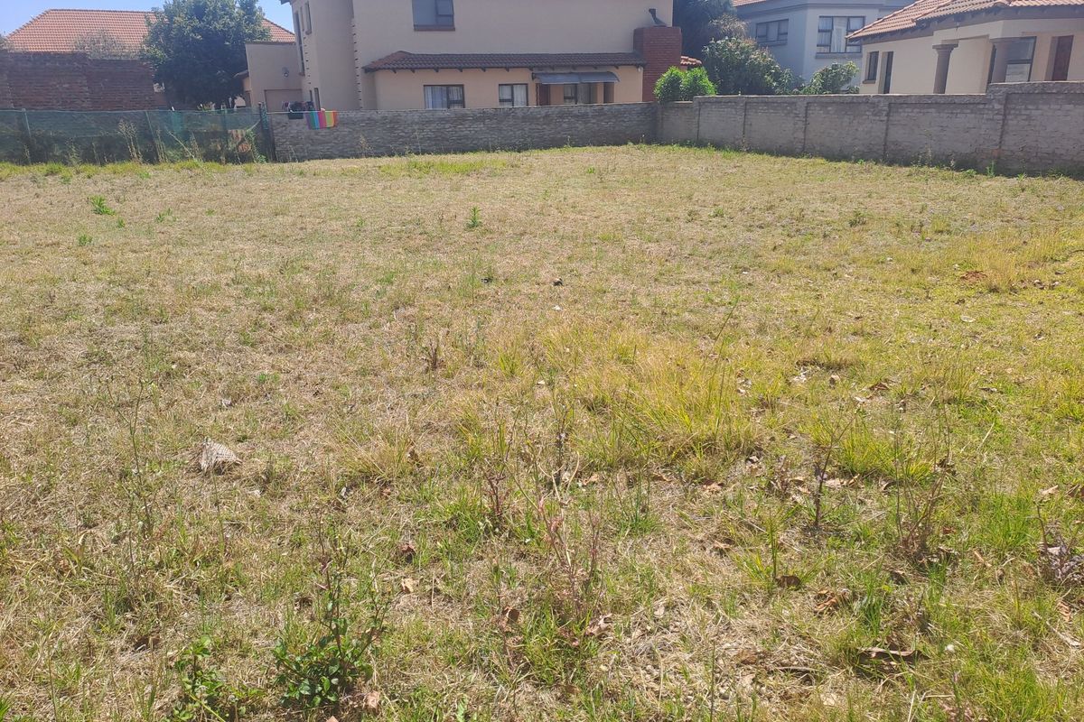 A vacant residential plot featuring a perimeter brick wall and natural grass coverage, situated in a developed neighborhood.