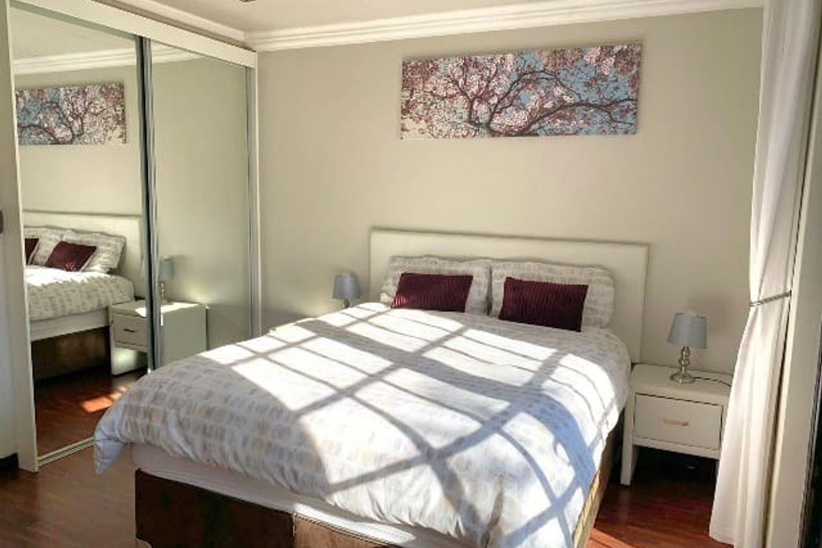 A well-maintained bedroom featuring laminate flooring, recessed downlights, and large mirrored sliding wardrobe doors that enhance the sense of space.