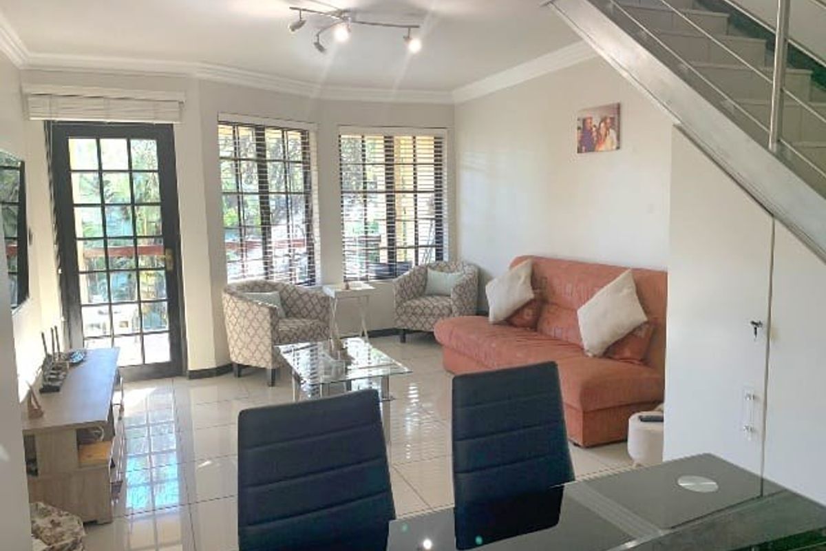 Open-plan living area featuring tiled floors, a staircase with stainless steel railings, and large windows providing natural light and access to the exterior.