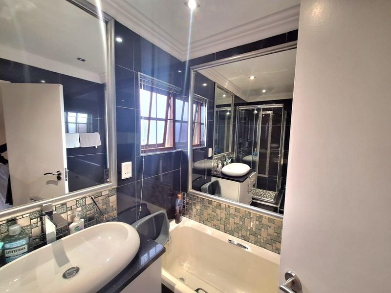 A modern bathroom featuring dark tiled walls, a built-in vanity with a vessel sink, a bathtub, and a separate glass-enclosed shower.