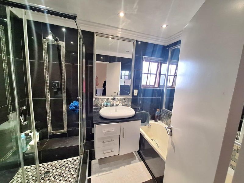 Modern bathroom featuring a glass-enclosed shower, a built-in vanity with a vessel sink, and a bathtub with dark tiled finishes.