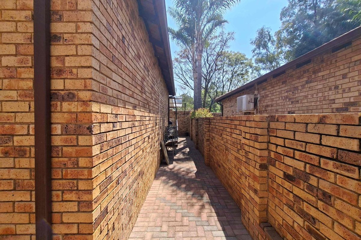 A narrow paved side walkway featuring face brick walls and an external air conditioning unit.