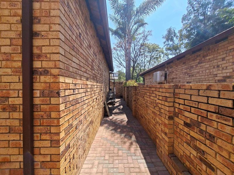 A narrow paved side walkway featuring face brick walls and an external air conditioning unit.