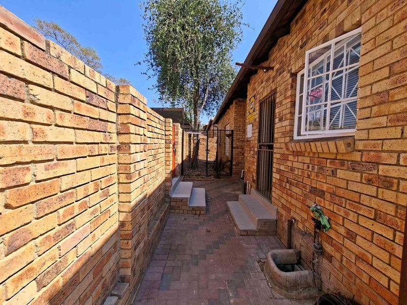 A side passage of the townhouse featuring face brick walls, paved flooring, and secure access points with security gates and bars.