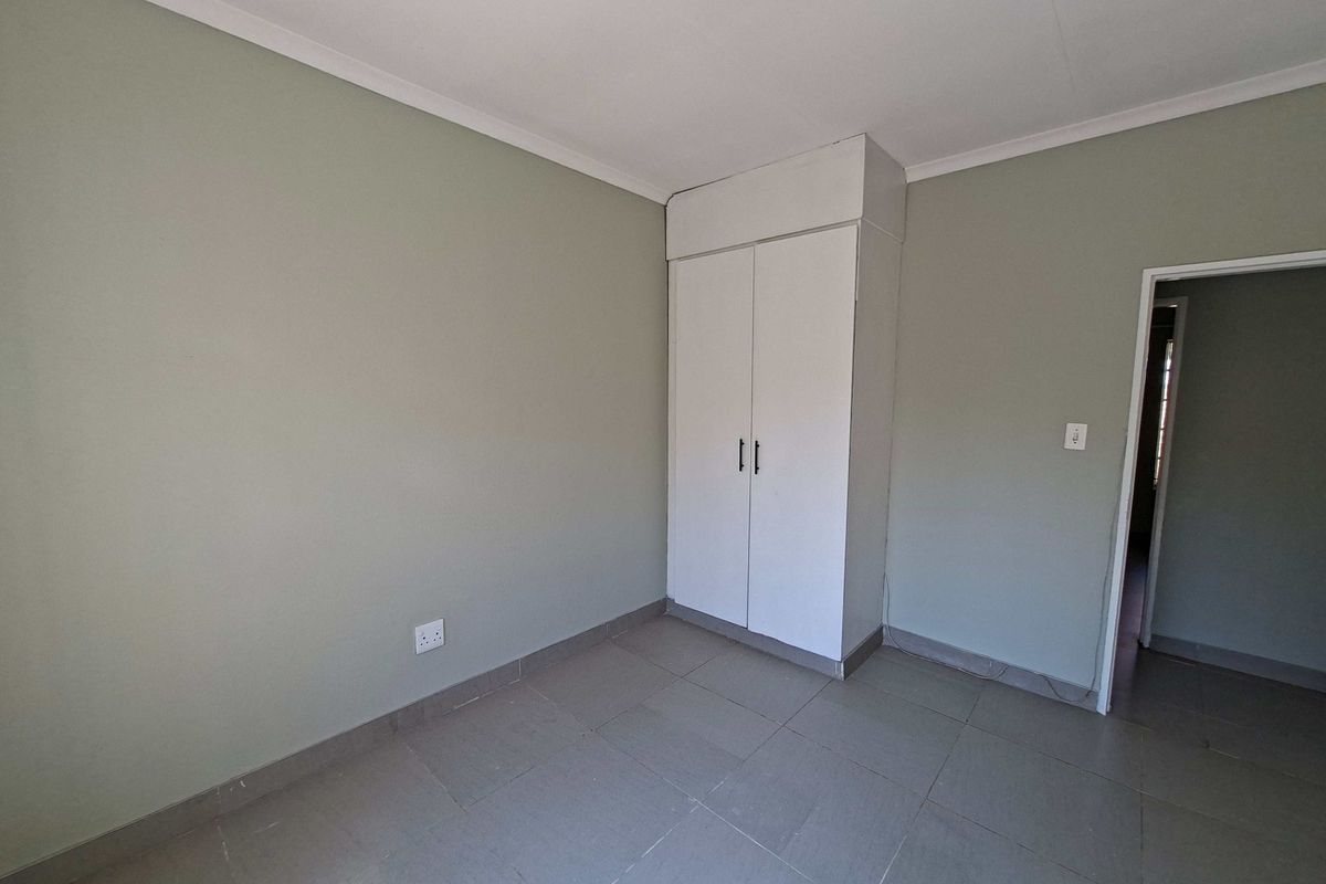 A clean, empty bedroom featuring neutral wall paint, tiled flooring, and a built-in wardrobe, offering a blank canvas for personalization.