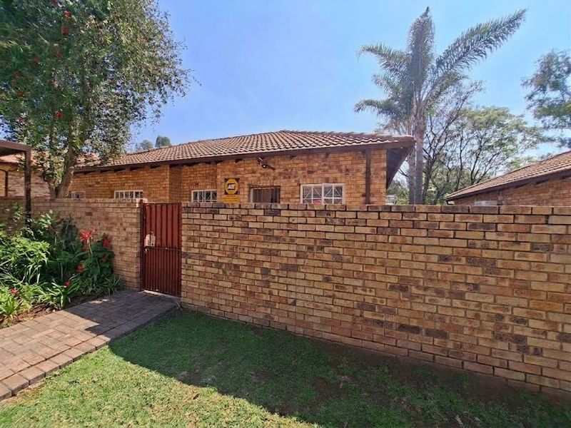 Front view of a face brick townhouse featuring a tiled roof, secure gated entrance, and a paved walkway leading to the property.