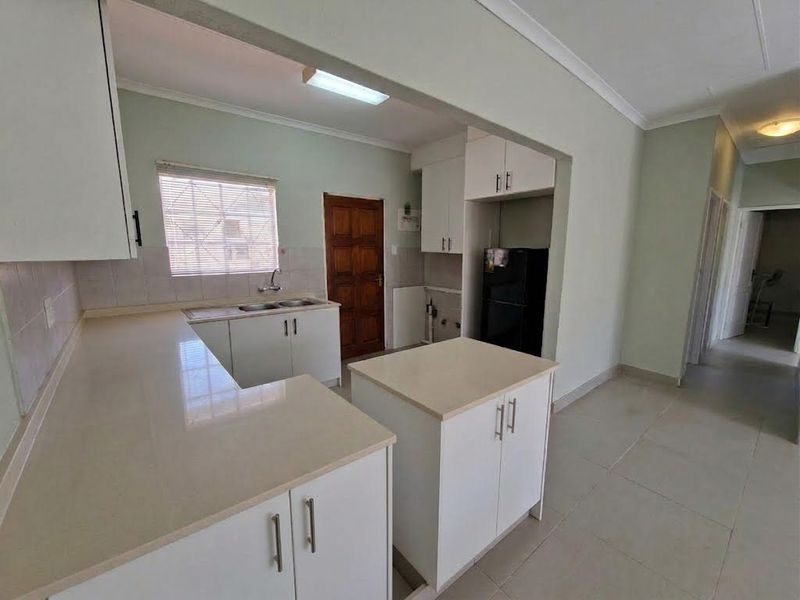 A functional kitchen featuring white built-in cabinetry, stone countertops, a central island, and tiled flooring, offering a clean and neutral space.