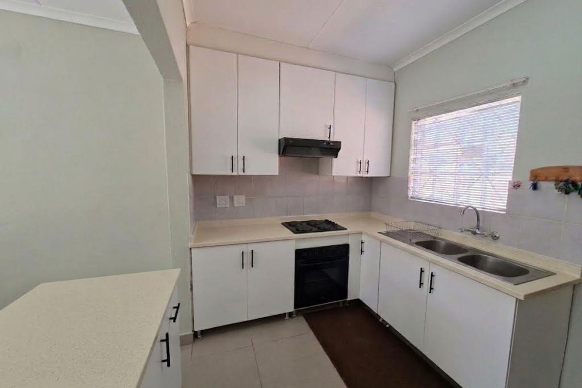 A functional kitchen featuring white built-in cabinetry, laminate countertops, a double sink, and integrated cooking appliances, offering a clean and practical workspace.