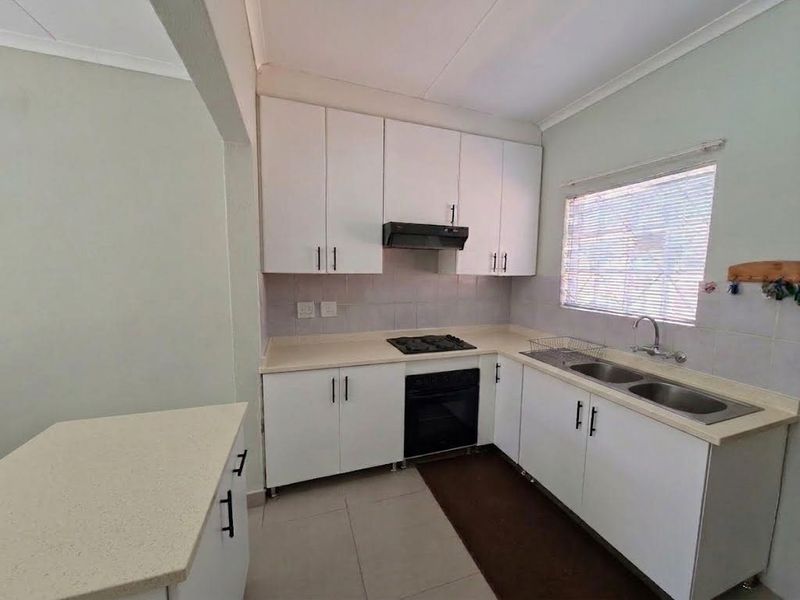 A functional kitchen featuring white built-in cabinetry, laminate countertops, a double sink, and integrated cooking appliances, offering a clean and practical workspace.